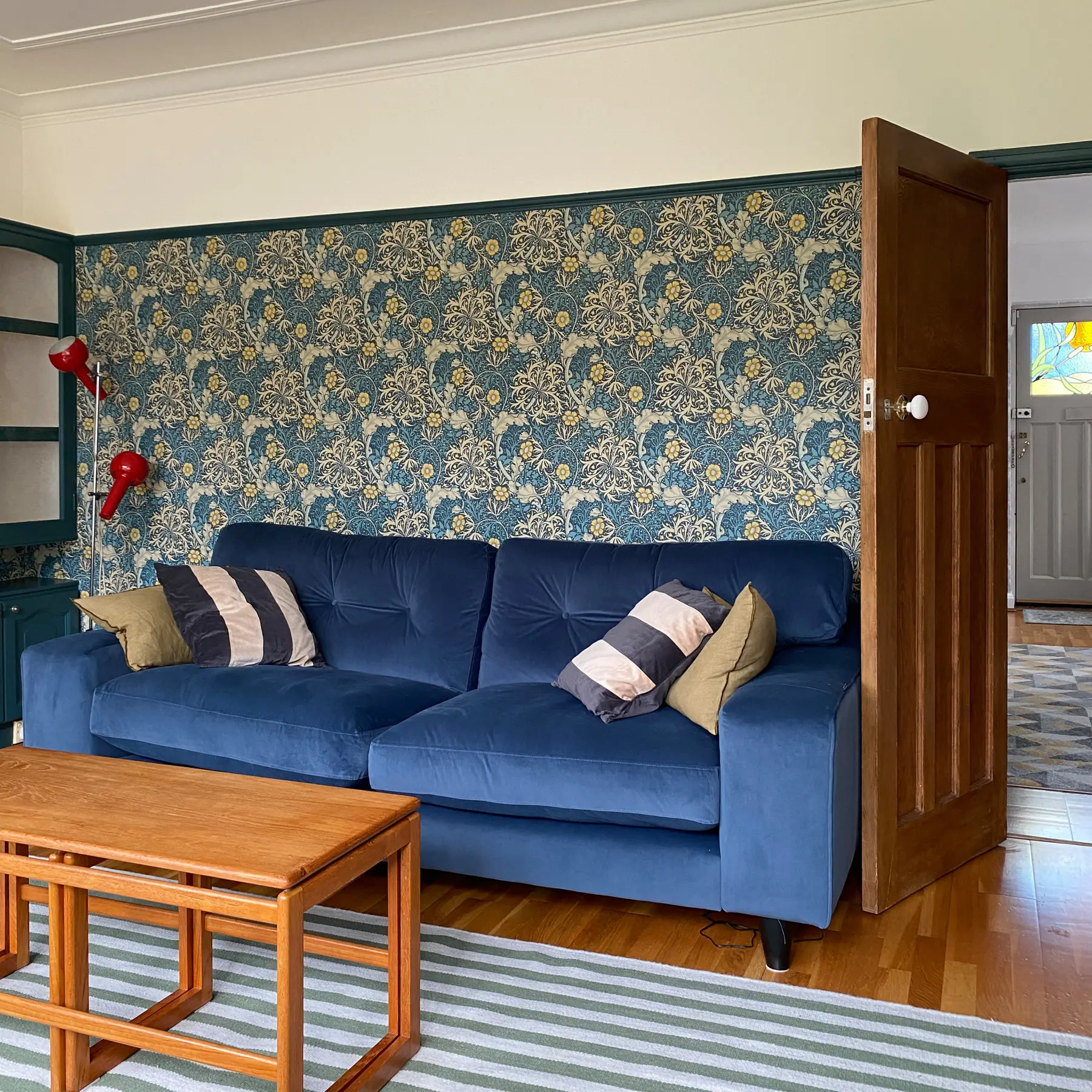 Navy velvet sofa with striped cushions beneath a William Morris wallpaper