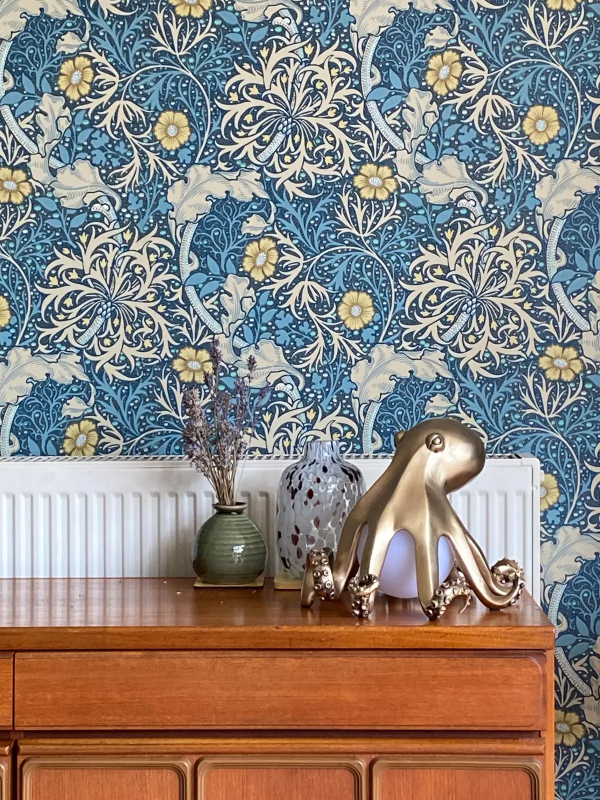 Blue Morris-pattern wallpaper styled with vases and a brass octopus ornament