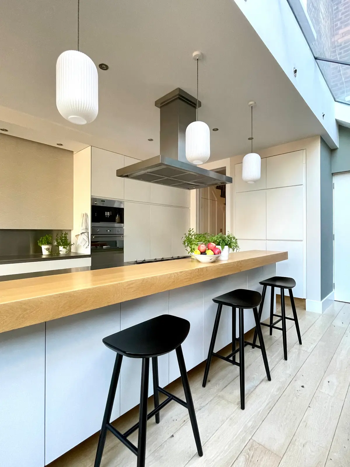 Kitchen island with an oak breakfast bar and black stools under a rooflight, East Finchley