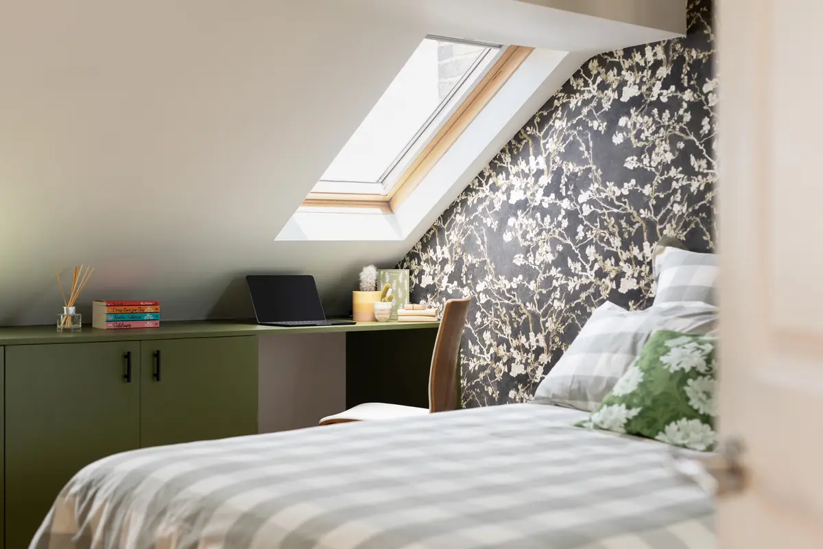 Loft bedroom under a skylight with dark botanical wallpaper and a sage desk