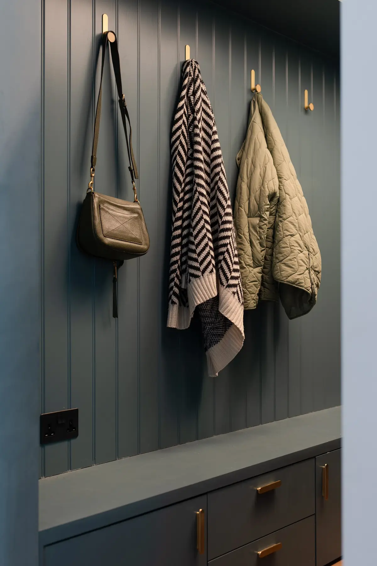 Hallway hooks with a bag and knitted scarves against dark green panelling