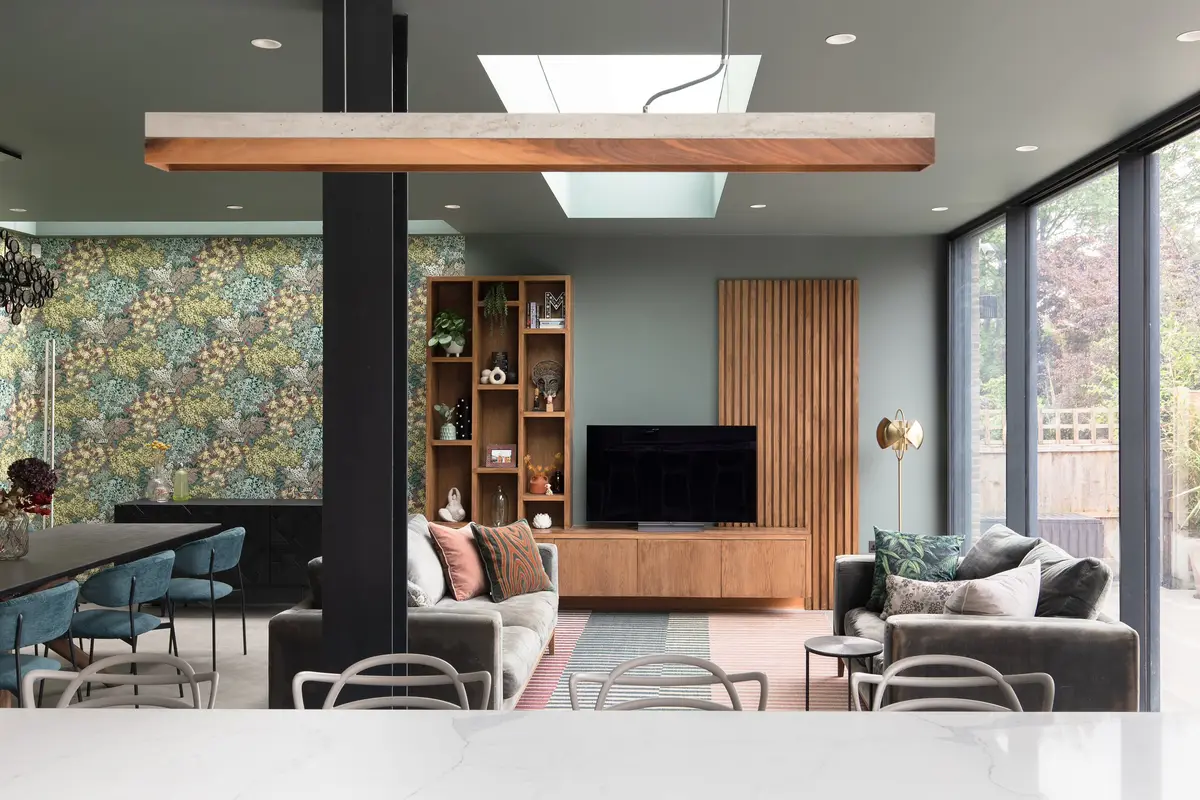 Open-plan extension with a feature wallpaper, oak shelving, dining table and sofa under a rooflight, Muswell Hill
