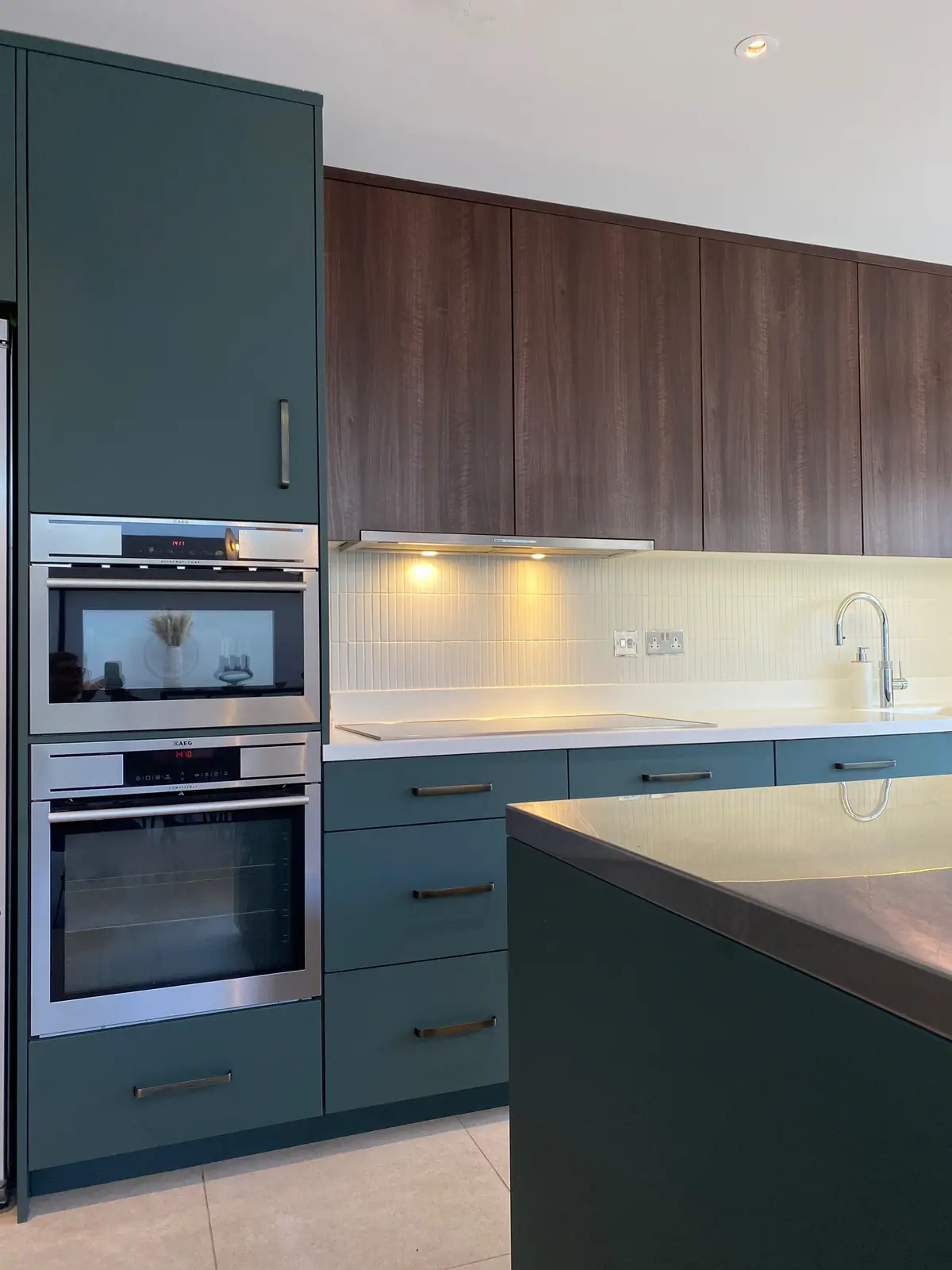 Teal and walnut kitchen with built-in ovens and a stone-topped island
