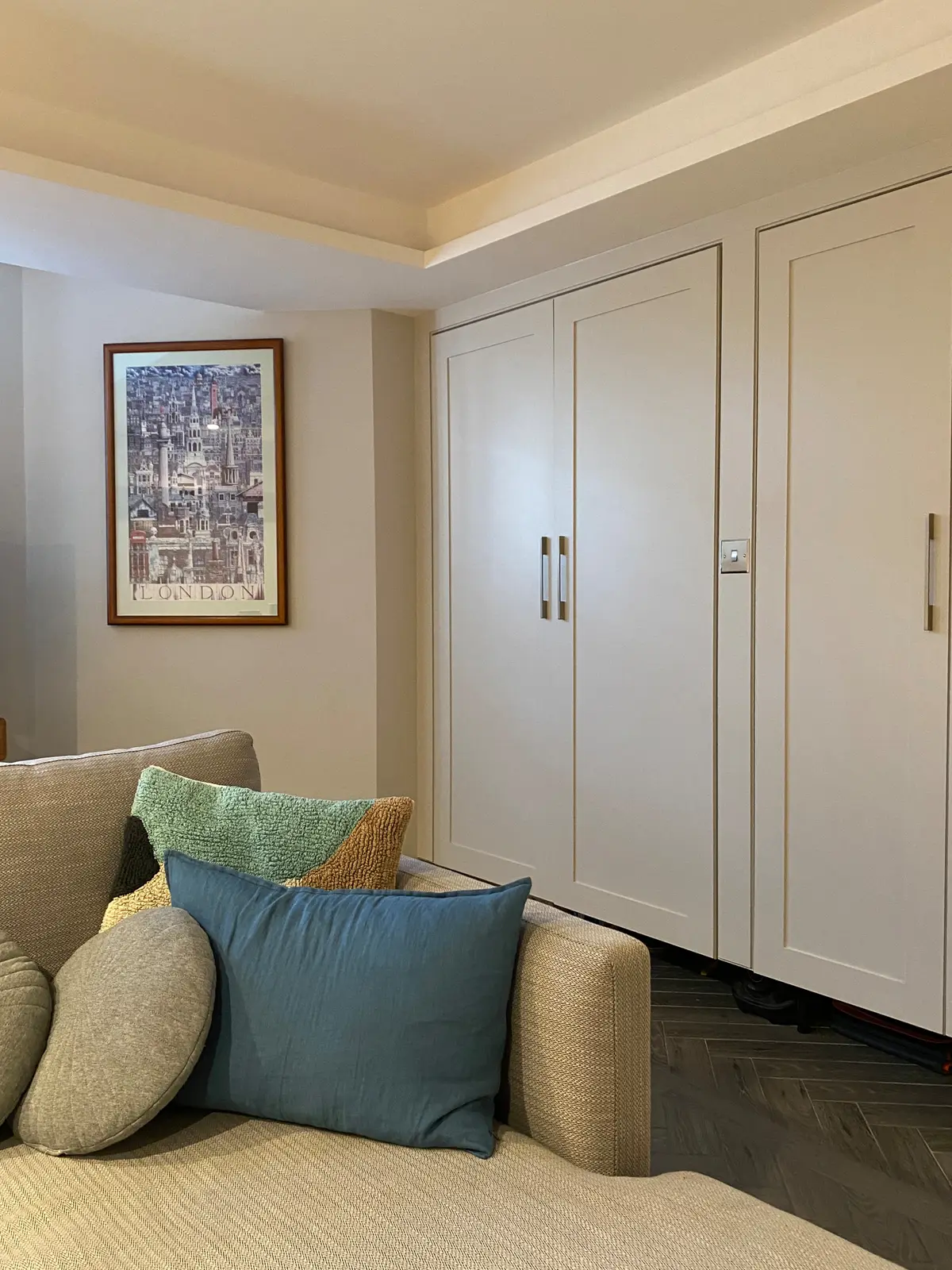 Basement den with cream built-in cupboards and a sofa with colourful cushions