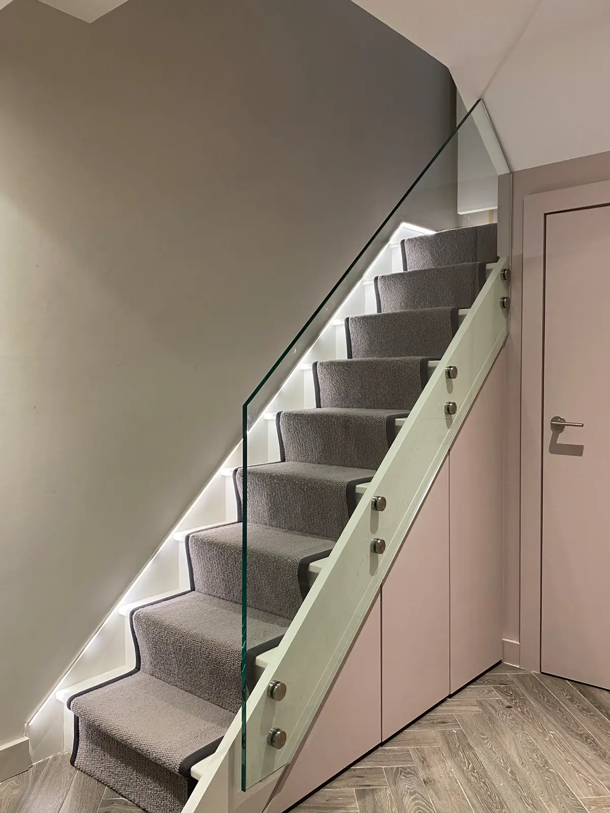 Basement staircase with a glass balustrade and lit treads