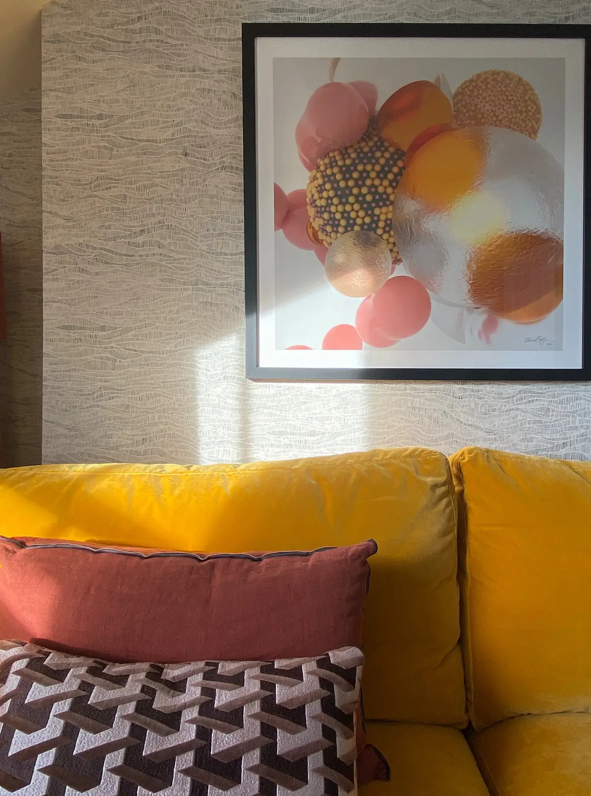 Mustard sofa below a large colourful print on grasscloth wallpaper