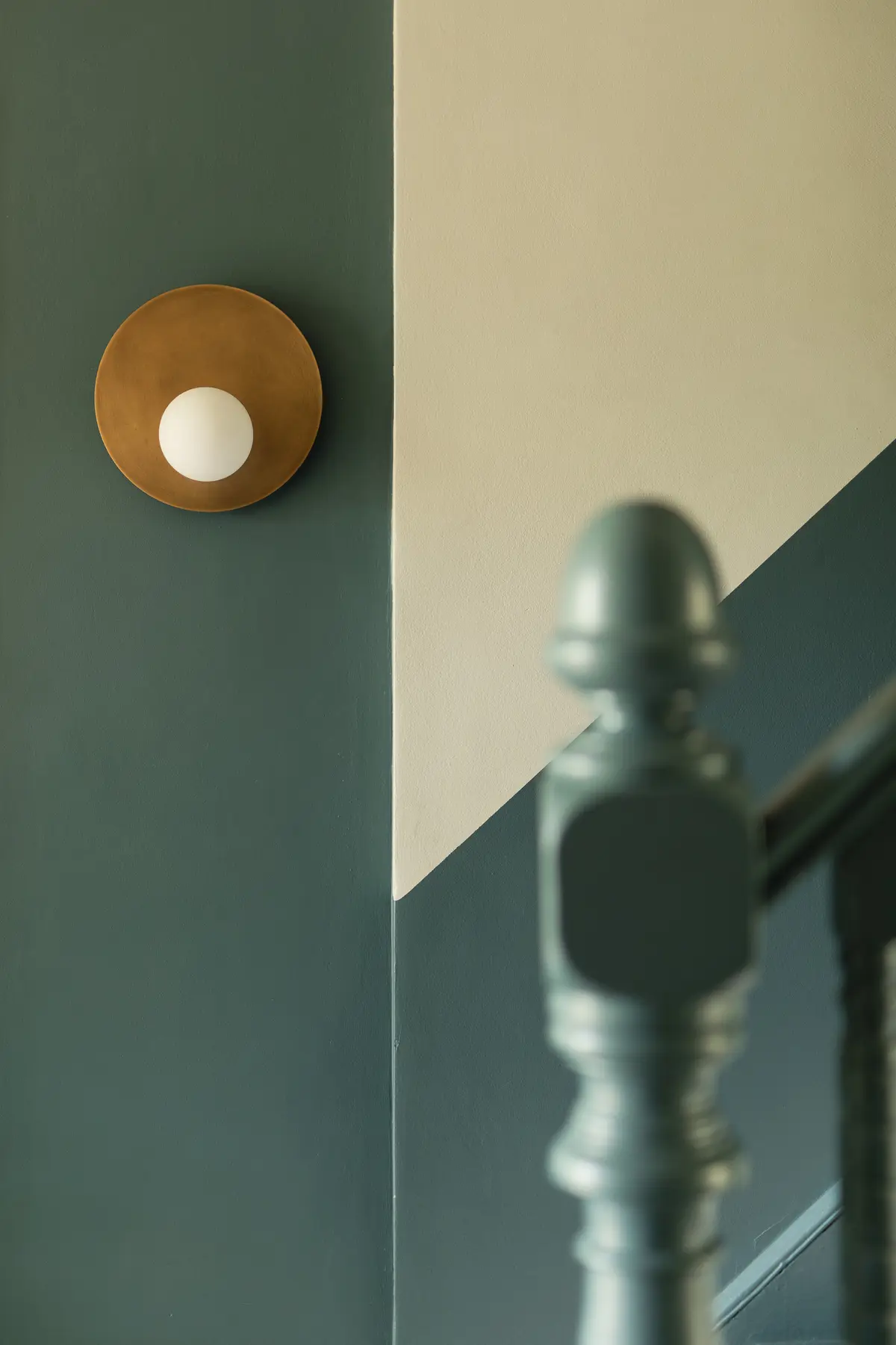 Teal staircase newel post and brass wall light against a two-tone painted wall