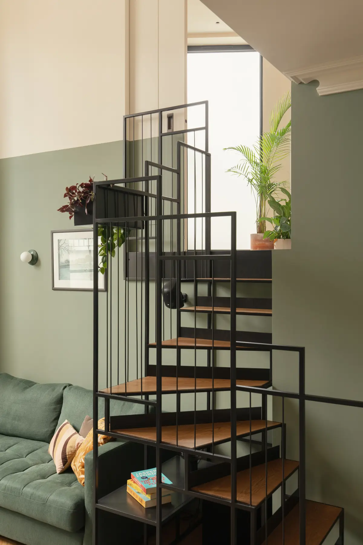 Green-painted stairwell with a black spiral staircase and trailing plants