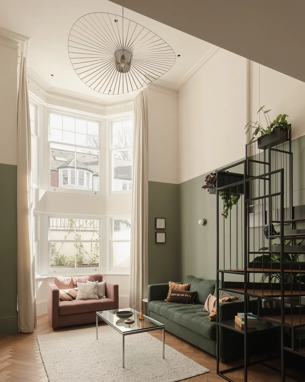 Bay window with shutters beside a green panelled wall and staircase