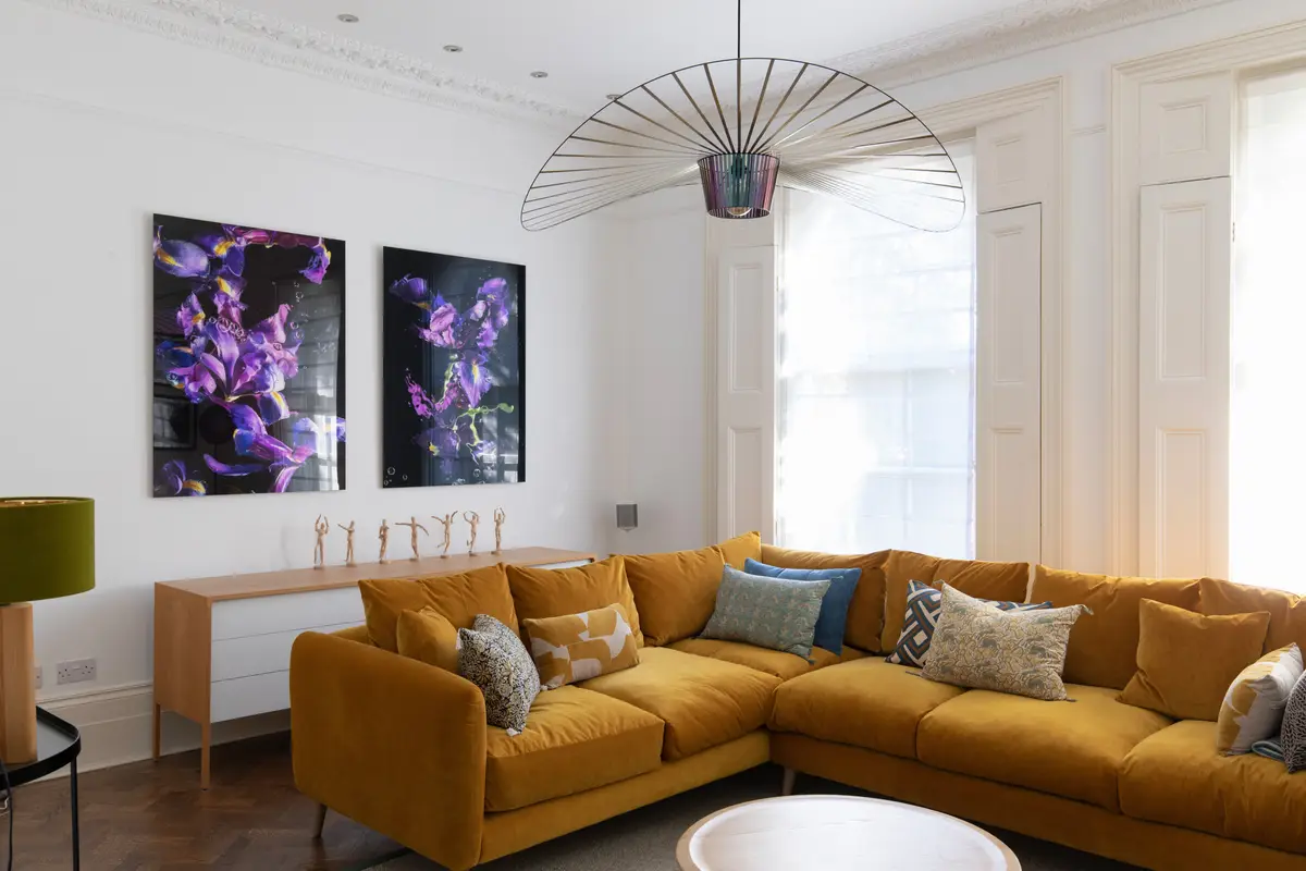 Georgian living room with a mustard corner sofa, oversized pendant and floral artworks, Canonbury