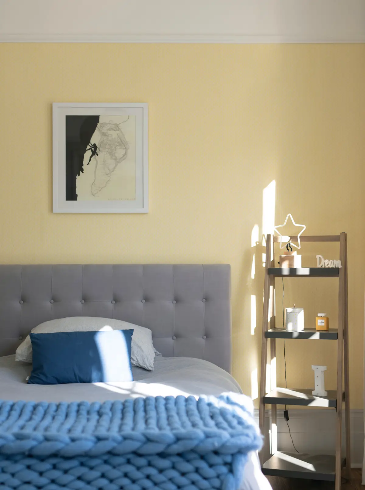Bedroom with a grey upholstered bed and blue throw against pale yellow walls