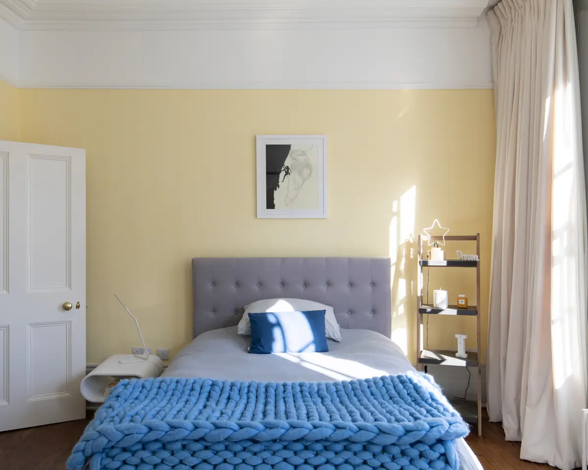 Pale yellow bedroom with a grey headboard and blue bedding