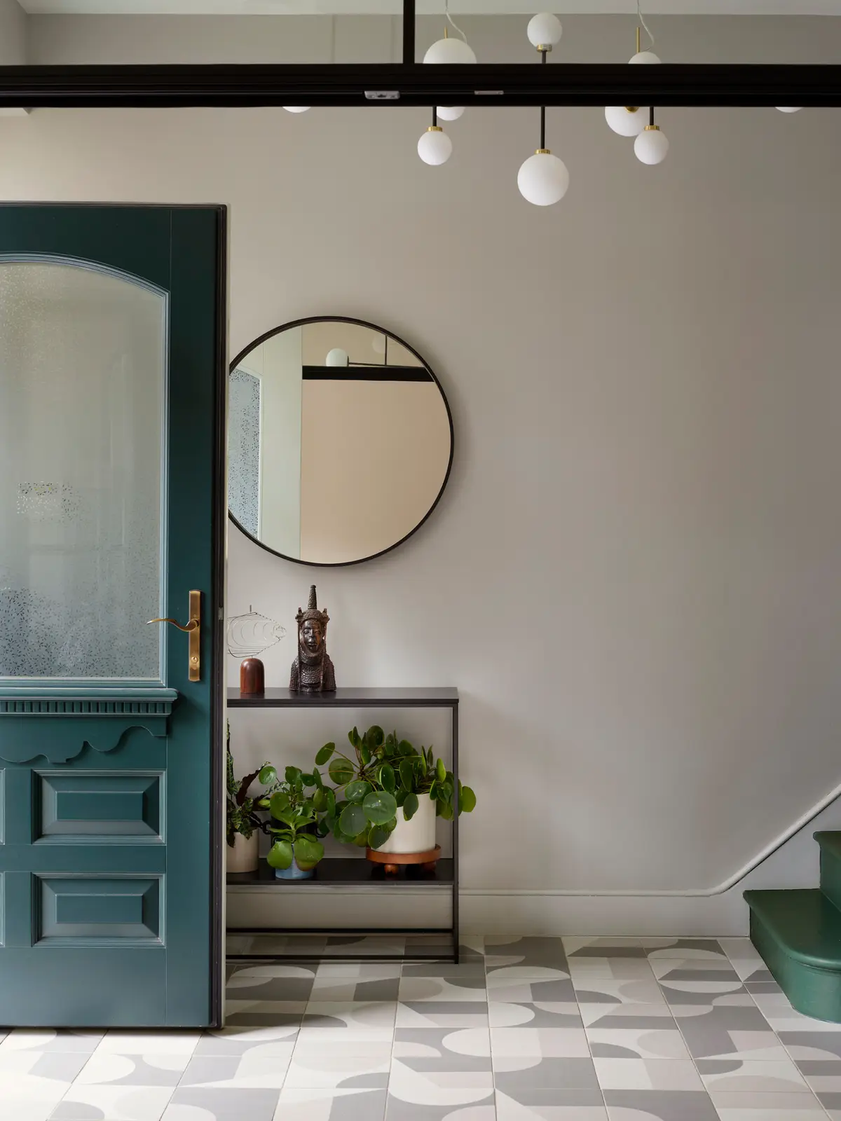 Entrance hall with a deep green front door, round mirror and plants