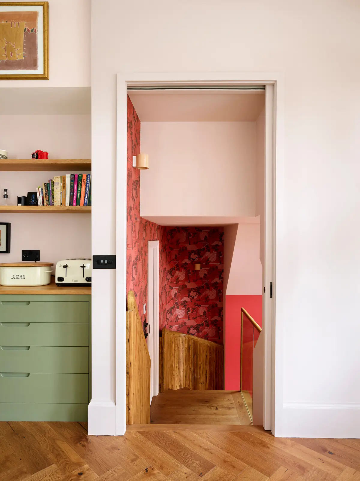 Pink and green kitchen corner with open shelves and a red-painted doorway