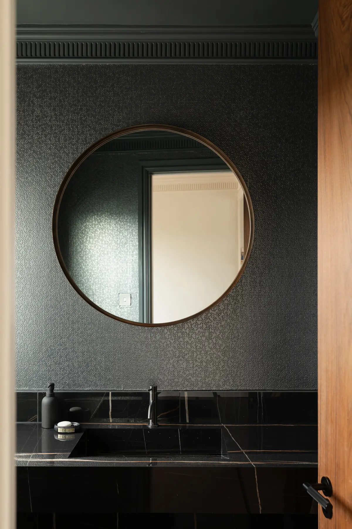 Round mirror on a dark textured wall in a cloakroom