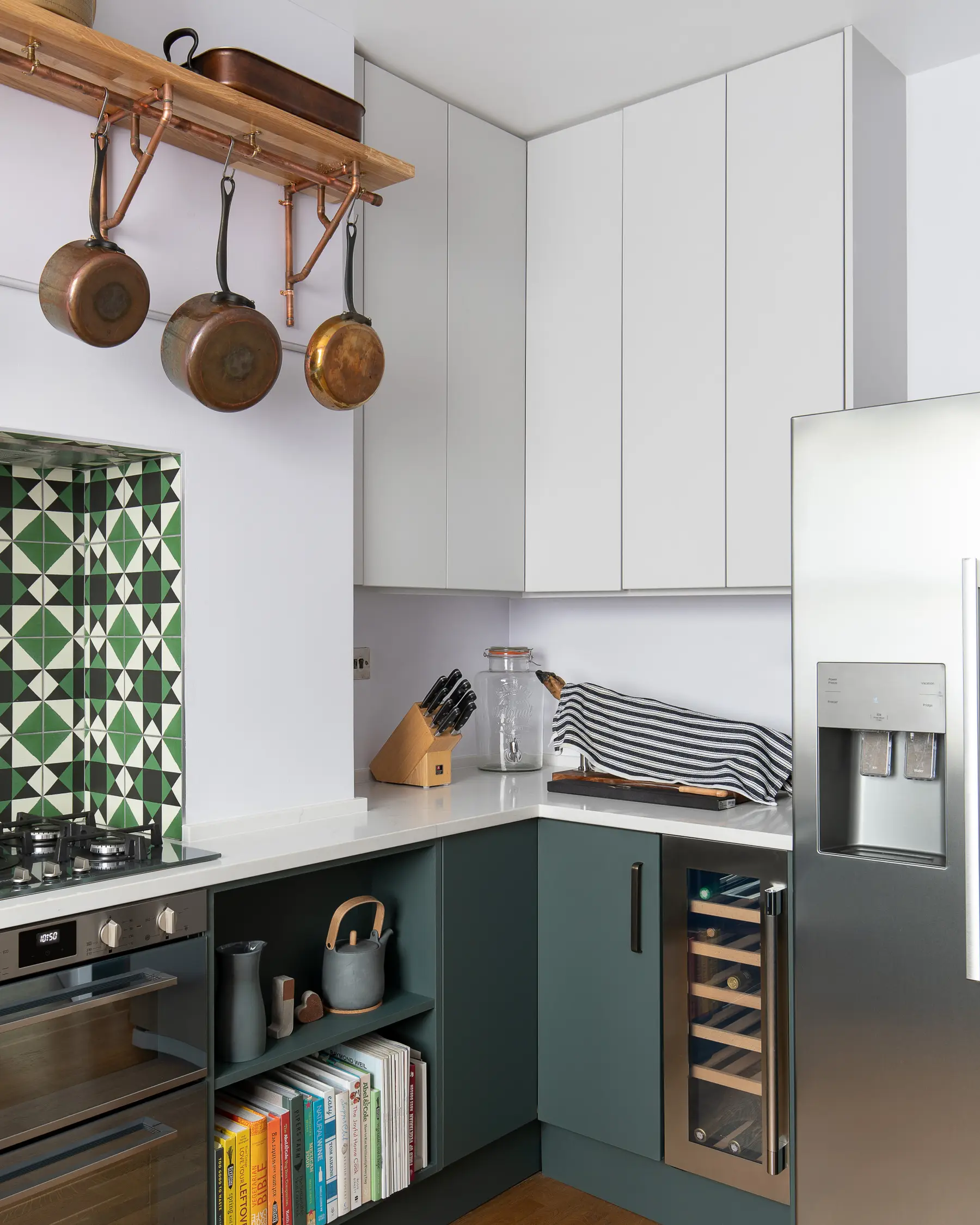 Kitchen with green geometric tiles, copper pans and white units