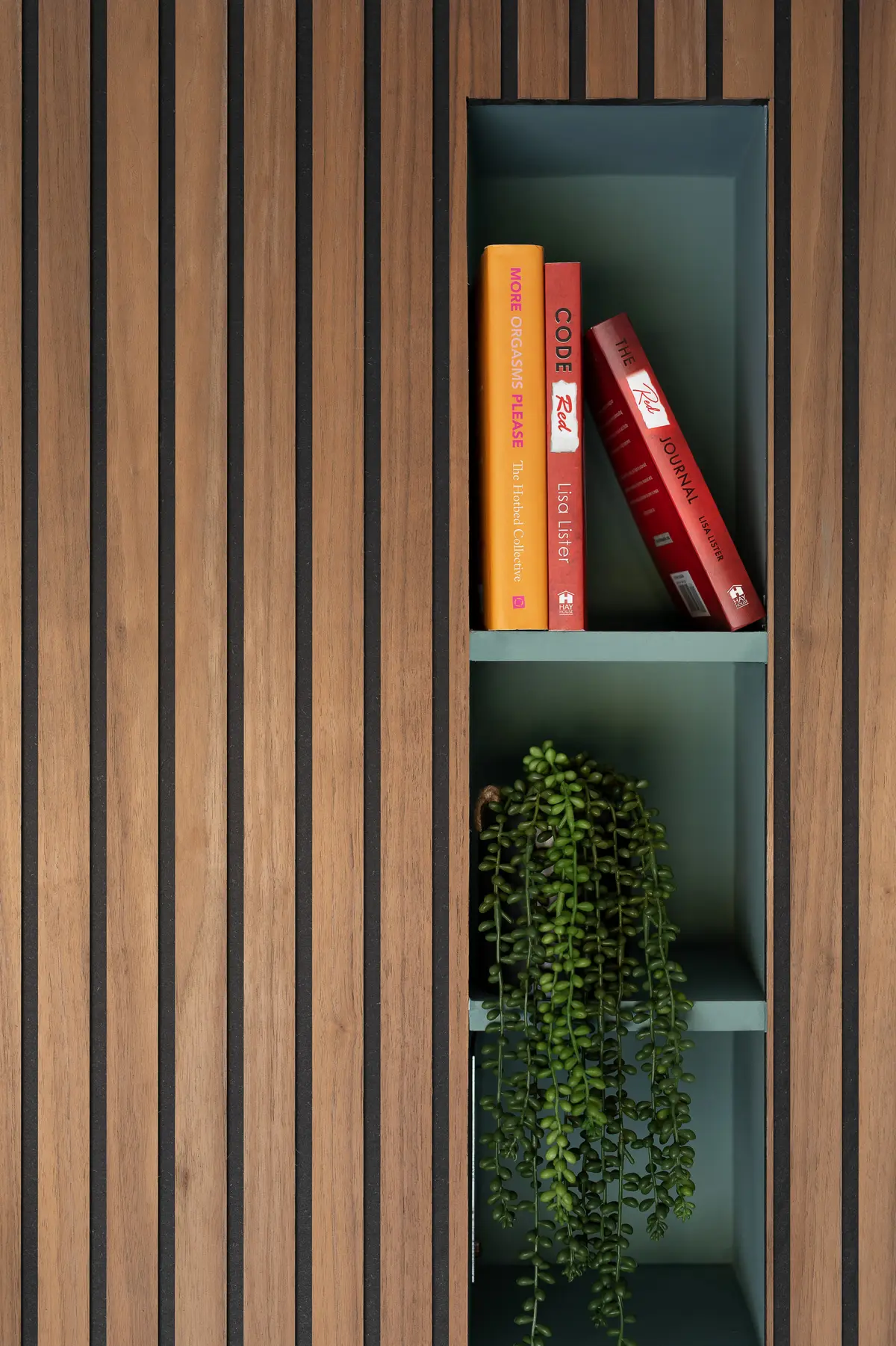 Oak slats framing green-painted open shelving with books