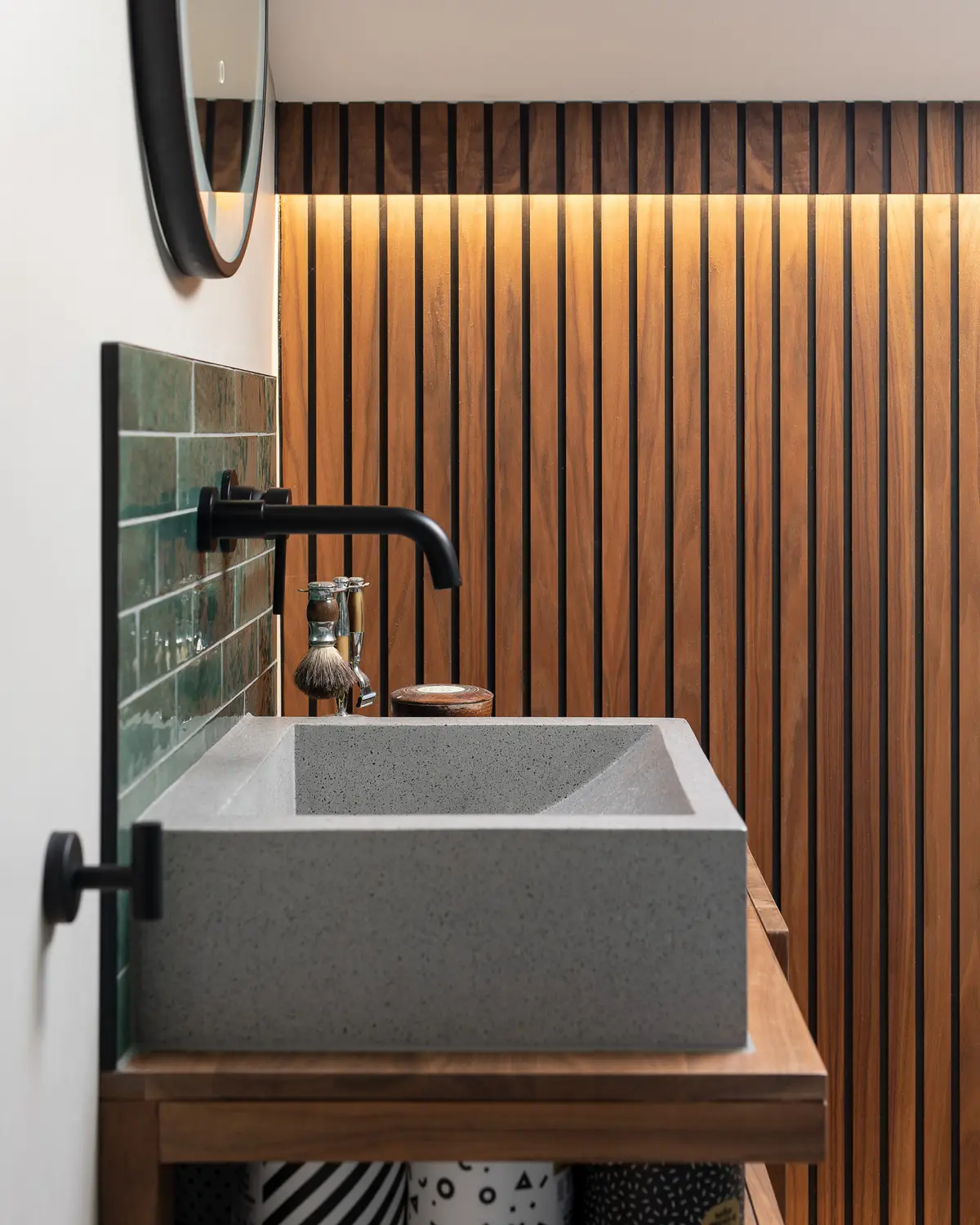 Concrete basin and black tap against oak slats and green tiles