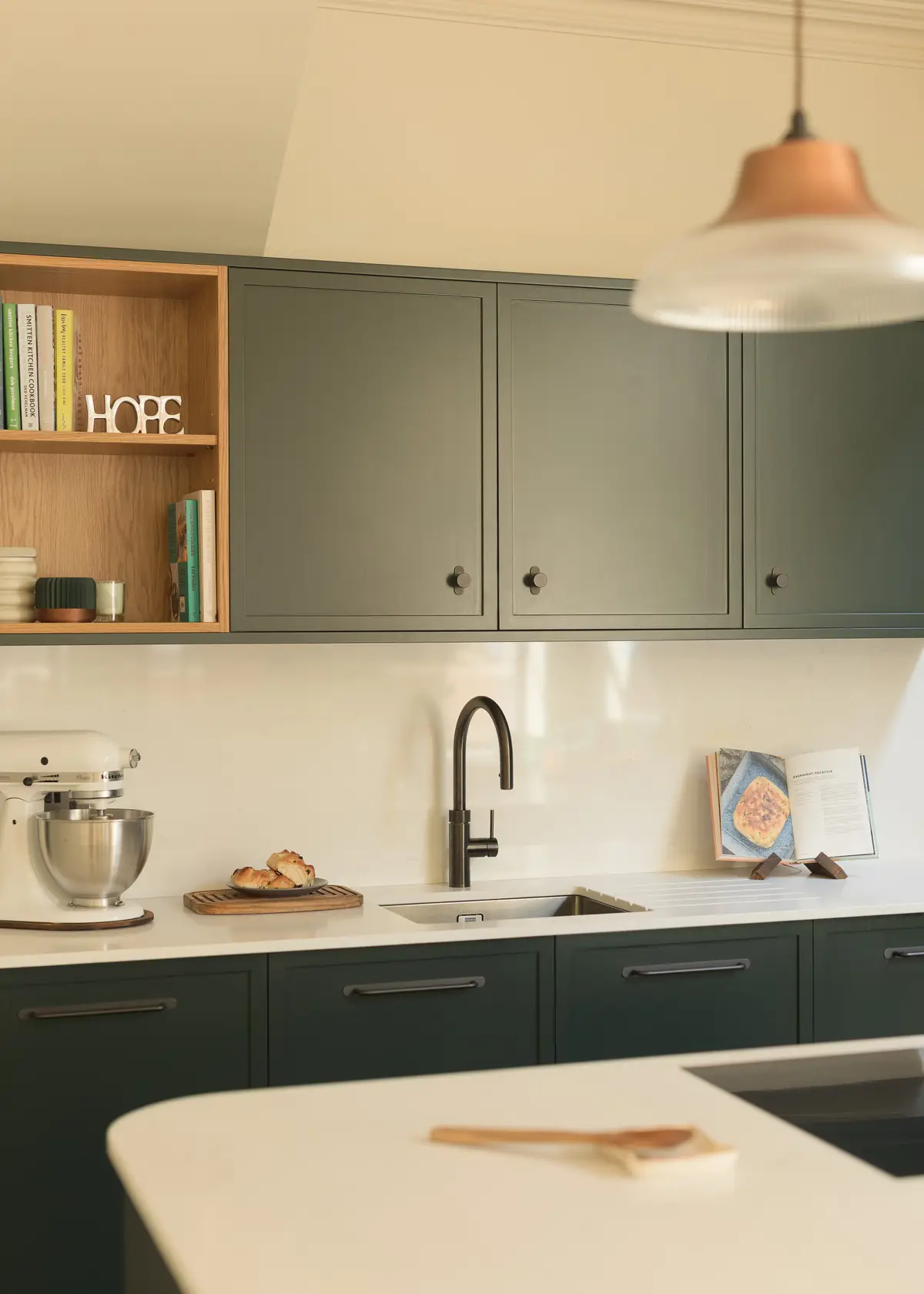 Sage green kitchen with a black tap and open oak shelving