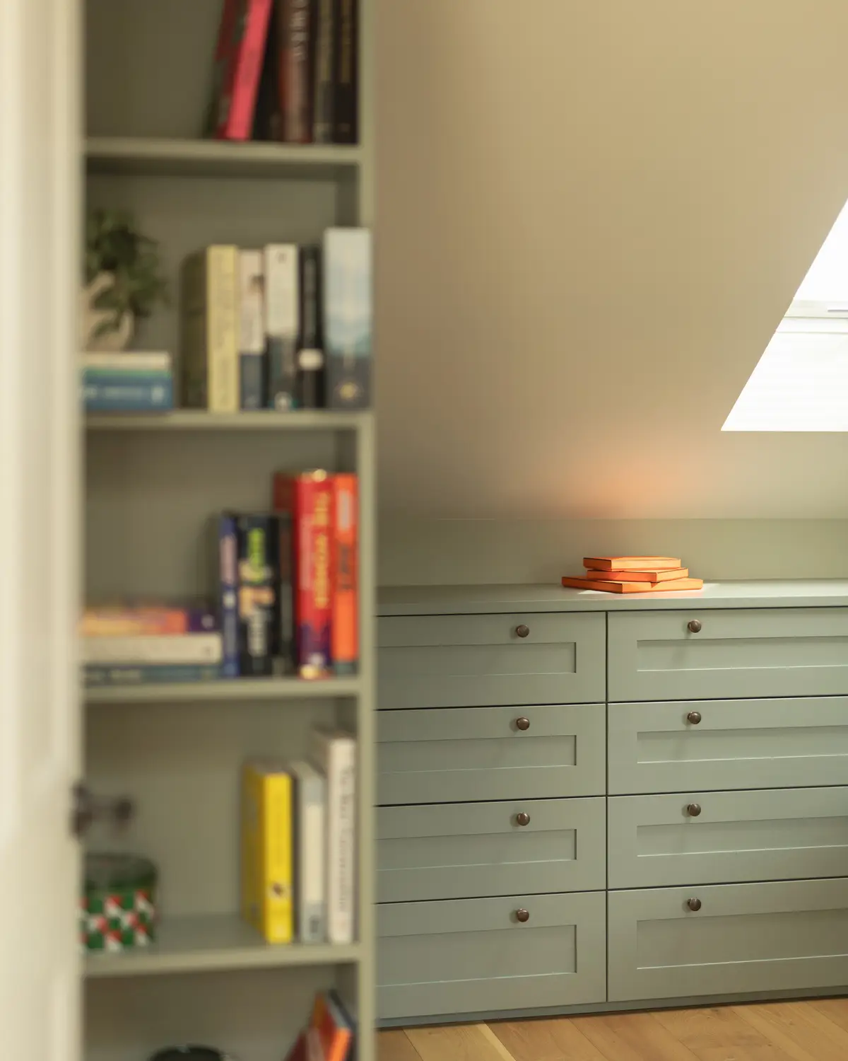 Loft alcove with built-in sage drawers and bookshelves under a skylight